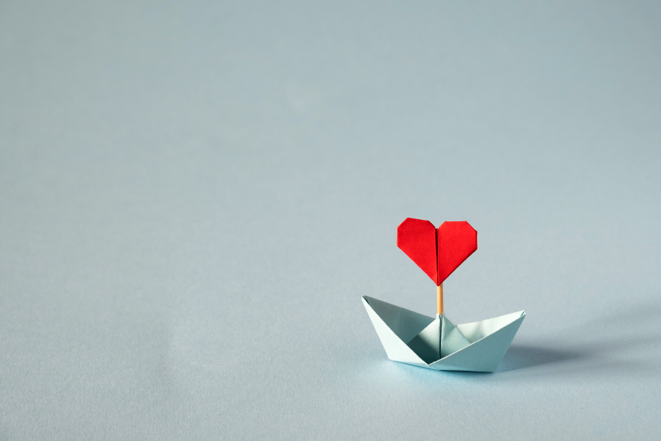 Origami boat with heart flag on glitter blue background